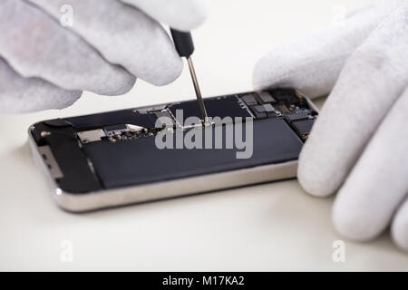 Nahaufnahme einer menschlichen Hand Instandsetzung Smartphone mit Schraubendreher Stockfoto