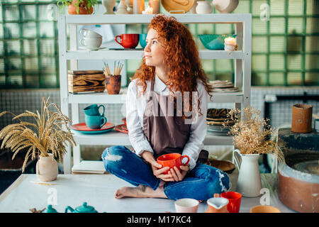 Rothaarige Frau sitzt im Lotussitz in Ton Shop Stockfoto