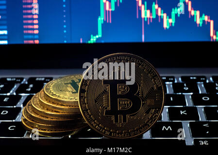 Minted Bitcoin cryptocurrency token Münze mehrere Münzen auf dem Computer Tastatur mit Kerzenhalter markt Grafik Grafik auf dem Bildschirm im Hintergrund gestapelt. Stockfoto