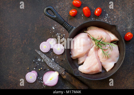 Frisches Fleisch. Rohes Hähnchenfilet in einer gusseisernen Pfanne, Gewürzen und frischem Rosmarin auf dem Küchentisch. Ansicht von oben mit einer Kopie. Stockfoto
