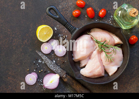 Frisches Fleisch. Rohes Hähnchenfilet in einer gusseisernen Pfanne, Gewürzen und frischem Rosmarin auf dem Küchentisch. Ansicht von oben mit einer Kopie. Stockfoto