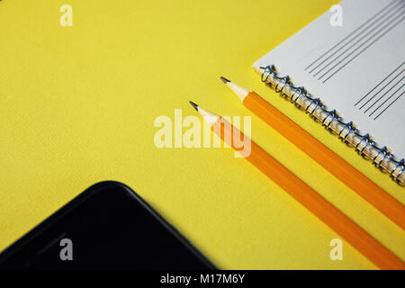 Bleistifte, Notebook und Handy auf gelbem Hintergrund. Stockfoto