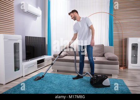 Junger Mann Reinigung blaue Teppiche mit Staubsauger zu Hause Stockfoto