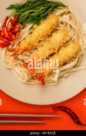 Im japanischen Stil Tempura Udon Nudeln Garnelen mit Chili und Frühlingszwiebeln auf rotem Hintergrund Stockfoto