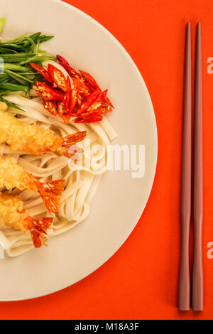 Im japanischen Stil Tempura Udon Nudeln Garnelen mit Chili und Frühlingszwiebeln auf rotem Hintergrund Stockfoto