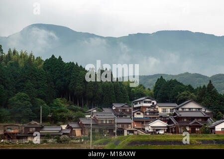 Blick auf die Häuser zusammen im ländlichen Japan überfüllt mit nebligen Berge und Bäume im Hintergrund und die reisfelder vor. Stockfoto