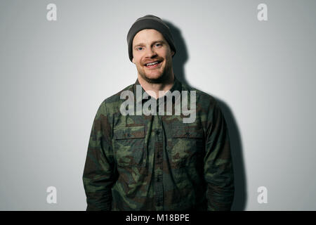 Jungen attraktiven Mann mit Camouflage Shirt und Hut auf grauem Hintergrund Stockfoto