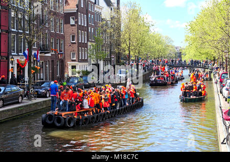 Eine Szene auf einem Kanal in Amsterdam auf des Königs Tag. Mehrere Boote im Kanal alle voller feiern Menschen tragen orange Farbe der Kleidung. Stockfoto