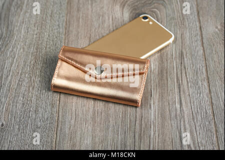 Golden Frau s Brieftasche legt mit mit einem IPhone auf einer hölzernen Oberfläche Stockfoto