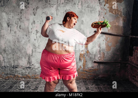 Übergewichtige Frau mit hantel und Sandwich in den Händen, Kampf gegen Fettleibigkeit, Übergewicht problem. Junk Food essen Stockfoto