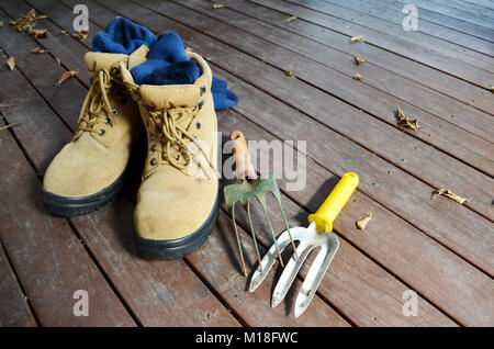 Paar Schuhe mit Garten Werkzeuge auf einem Holzdeck Stockfoto