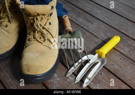 Paar Schuhe mit Garten Werkzeuge auf einem Holzdeck Stockfoto