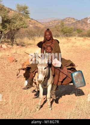 Junge, verheiratete Himbafrau Fahrten mit einem kleinen Kind auf einem Esel, Kaokoveld, Namibia Stockfoto