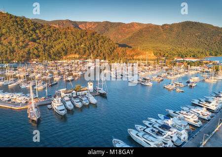 Luftaufnahme von Booten und Yachten bei Sonnenuntergang in der Türkei. Bunte Landschaft mit Yachten in der Marina Bay, Meer, Berge, Wald, blauer Himmel. Ansicht von oben von Dron Stockfoto
