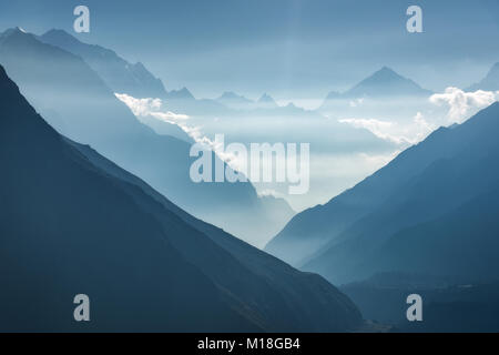 Majestätischen Blick auf die Silhouetten der Berge und niedrige Wolken bei Sonnenuntergang in Nepal. Landschaft mit hohen Felsen der Berge des Himalaja, schönen blauen Himmel und Stockfoto