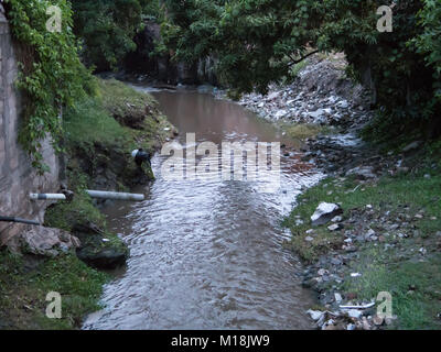 Holguin, Kuba - 31. August 2017: schlammigen Bach mit sichtbaren Papierkorb auf den Seiten gesehen Langsam. Stockfoto