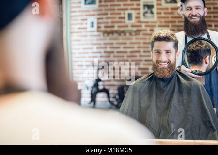 Junger Mann lächelnd, während sie an seiner neuen trendigen Haarschnitt in der Stockfoto