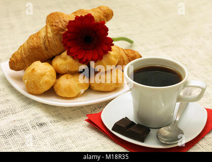 Eine Tasse Kaffee am Morgen vor dem Hintergrund der weißen Tischdecken und Platten aus Croissants und Windbeutel Stockfoto