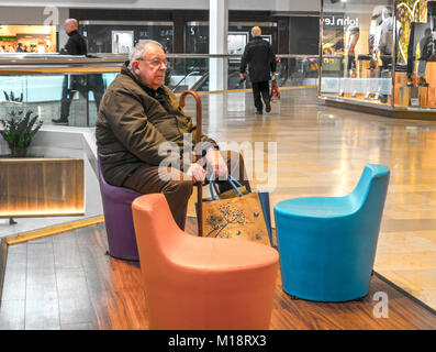 Alter Mann, sitzend, mit einem Stock und einige Tragetaschen in die Queensgate Shopping Center, Stadt Peterborough, Cambridgeshire, England, UK. Stockfoto