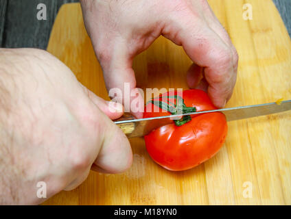 Ein Mann mit einem großen Messer schneiden eine reife Tomate in zwei Teile. Stockfoto