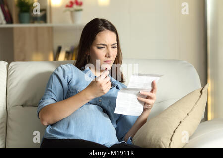 Schwangere Frau mit einem Merkblatt verwirrt Vor nehmen Sie eine Pille sitzen auf einer Couch im Wohnzimmer zu Hause Stockfoto