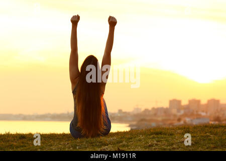 Zurück Hintergrundlicht Porträt einer aufgeregt, einzelne Frau Anheben der Arme den Sonnenuntergang über der Stadt mit einem warmen Licht im Hintergrund anzeigen Stockfoto