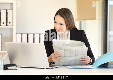 Executive vergleich News online in einem Laptop und eine Zeitung im Büro Stockfoto