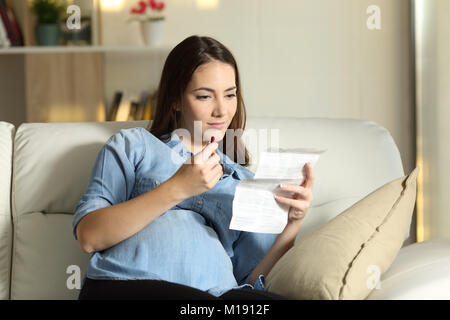 Schwangere Frau liest eine Packungsbeilage vor nehmen Sie eine Pille sitzen auf einer Couch im Wohnzimmer zu Hause Stockfoto