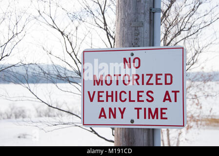 Rote und weiße Zeichen in Parkstellung angibt, keine motorisierten Fahrzeuge jederzeit in der Spekulant, NY USA im Winter, mit Schnee und gefrorenen See im Hintergrund. Stockfoto