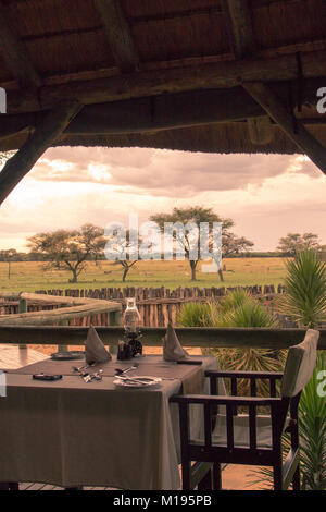 Tisch für das Abendessen für zwei mit Blick auf die afrikanische Savanne bei Sonnenuntergang. Stockfoto