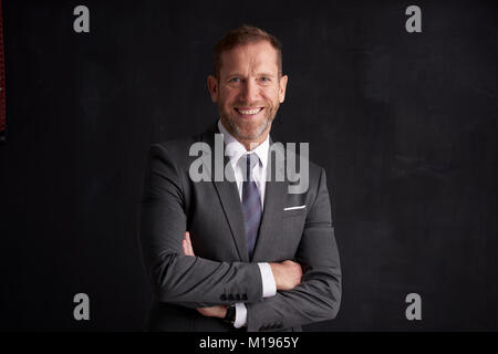 Portraitfotos von einer glücklichen Financial Director Geschäftsmann tragen Anzug und mit Waffen auf dunklem Hintergrund gekreuzt. Stockfoto