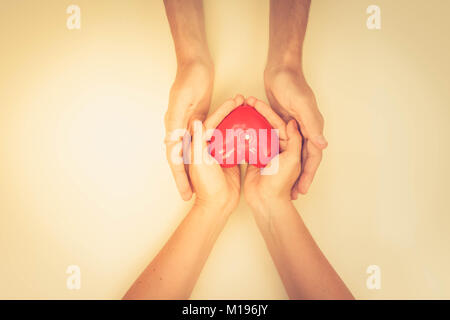 Zwei Paare von someones Hände halten roten Burning Heart, Ansicht von oben, Retro getönt Stockfoto