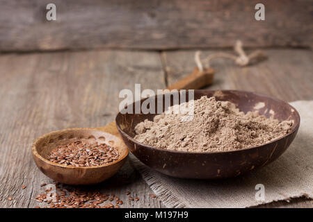 Flachs Mehl (Glutenfrei) in eine Schüssel geben, Leinsamen in einem hölzernen Löffel auf alten hölzernen Hintergrund Stockfoto
