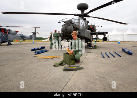 Britische Armee AH-64 Apache mit Krewman, das Waffenschalen in einen Munitionskasten lädt. Waffen. Verteidigungsindustrie. Militärangehörige, Besatzung Stockfoto