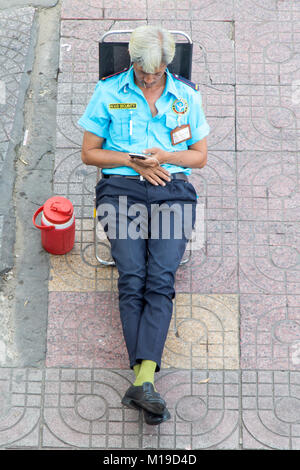 SAIGON, VIETNAM, 17.12.2017, Sicherheit Mann sitzt auf der Straße und mit Blick auf sein Handy. Stockfoto