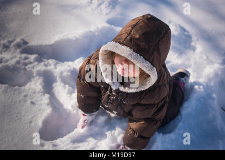 Auf der Suche nach einer 3-jährigen Kleinkind Mädchen mit einem wintermantel und Sitzen im Schnee. Stockfoto