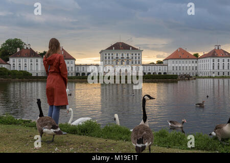 Dramatische Kulisse von Schloss Nymphenburg in München Deutschland. Sonnenuntergang nach der sorm. Frau weiße Schwäne füttern und duks Schwimmen im Teich vor Der p Stockfoto