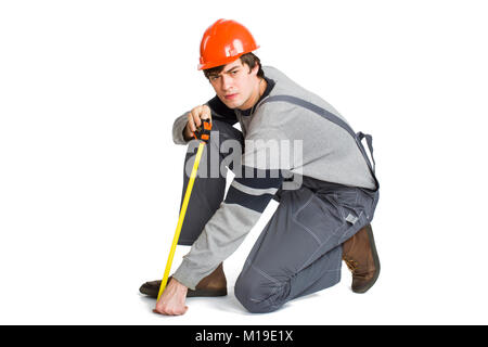 Ein junger Mann, der in der grauen Kleidung und orange-Helm Messung der metrische Raum im Zimmer. Stockfoto