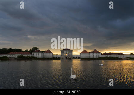 Dramatische Kulisse von Schloss Nymphenburg in München Deutschland. Sonnenuntergang nach der sorm. Weiße Schwäne und duks Schwimmen im Teich vor dem Palast. Stockfoto