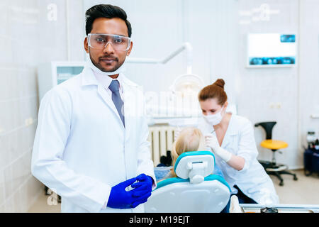 Zahnarzt prüfen Patienten Zähne Porträt einer jungen zuversichtlich indischen männlichen Zahnarzt in der Klinik vor der Frau Doktor, Prüfung der Zähne des Patienten. Stockfoto