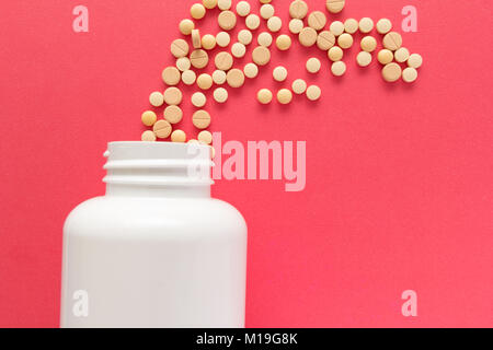 Gruppe der sortierten beige Tabletten. Kapseln verschütten aus weiße Flasche. Roten Hintergrund. Leitung, Art Kurs Konzept. Stockfoto