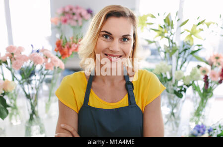 Schöne Frau florist im Blumengeschäft. Weibliche Blumenhändler in Schürze stand mit verschränkten Armen und Kamera. Stockfoto