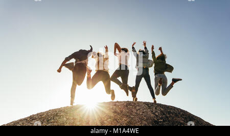 Ansicht der Rückseite des Gruppe von glücklich, Freunde, Spaß am Berg. Männer und Frauen springen auf Mountain Top gegen Sonnenuntergang. Stockfoto