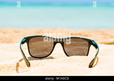 Schwarze Sonnenbrille auf Sand am Strand im Sommer Stockfoto