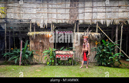 Junge bornesischen Mann mit einem Tribal Kostüm vor einer traditionellen longhouse, Mari Mari Cultural Village, Kota Kinabalu, Sabah, Borneo, Malaysia Stockfoto