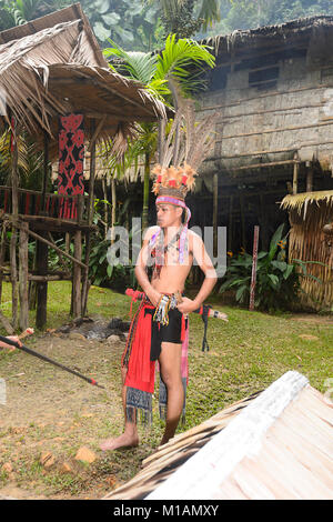 Junge bornesischen Mann mit Tribal Dekorationen vor einem traditionellen Langhaus, Mari Mari Cultural Village, Kota Kinabalu, Sabah, Borneo, Malaysia Stockfoto