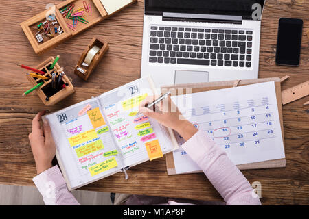 Nahaufnahme der Geschäftsfrau Schreiben Termine im Kalender Tagebuch auf Schreibtisch Stockfoto