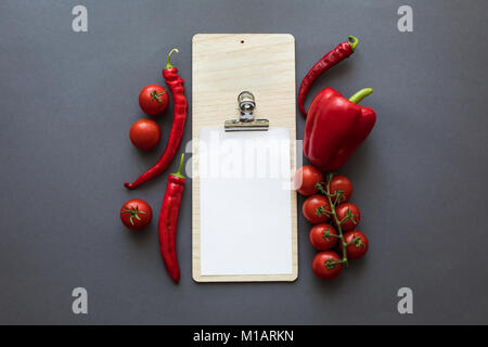 Blick von oben auf die frische reife rote Paprika und Tomaten mit leeren Blatt Papier auf Grau Stockfoto