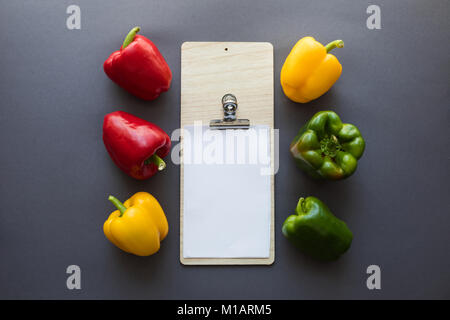 Blick von oben auf die verschiedenen frischen Paprika mit leeren Zwischenablage und Schneidbrett auf Grau Stockfoto