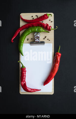 Blick von oben auf die chili peppers mit Samen und ein leeres Blatt Papier auf Zwischenablage isoliert auf Schwarz Stockfoto